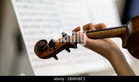 Geigerin spielt eine antike Barockgeige in Nahaufnahme über der Schulter mit der Hand auf den Saiten vor dem Hintergrund einer Partitur Stockfoto