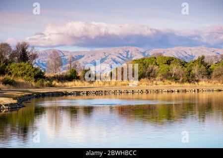 Blick auf den Sonnenuntergang auf den Shoreline Lake, mit Bäumen, die sich in der ruhigen Wasseroberfläche spiegeln; Diablo Mountain Range im Hintergrund sichtbar; Mountain View, South Stockfoto