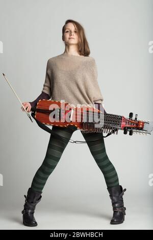 Stolze junge Frau mit einer modernen Reproduktion der traditionellen schwedischen mittelalterlichen Nyckelharpa in einem vollen Porträt über grau Stockfoto