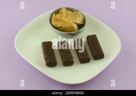 Dunkle Schokolade Erdnussbutter Wafer Cookies auf weißem Teller und Erdnussbutter in Tauchschüssel auf Lavendel Hintergrund Stockfoto