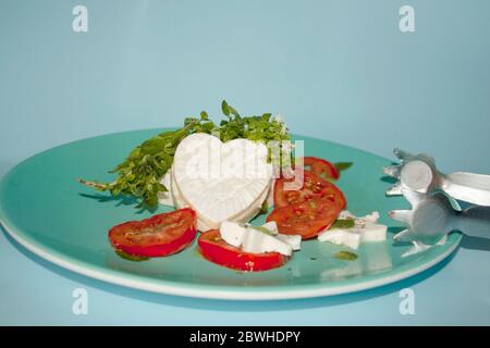 Frischer Basilikum, der herzförmigen Brie-Käse auf einem Salatteller mit Tomatenscheiben und sternförmigen Panelakäsen garniert Stockfoto