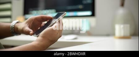 Seitenansicht des männlichen Unternehmers mit Smartphone während sitzen am Arbeitstisch in verschwommenem Büroraum Hintergrund Stockfoto