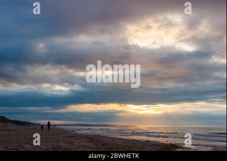 Entspannender Abend am Strand. Mutter und Tochter schlendern am Ufer. Sonnenstrahlen, die durch Öffnungen in Wolken leuchten. Cavendish Beach, PEI, Kanada. Stockfoto