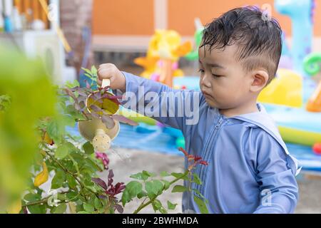 Asiatische niedlich liebenswert kleinen Kleinkind junge in Bewässerung Bäume Topf mit kleinen Dose im Freien. Spaß Baby Gartenarbeit Pflanze im Hinterhof Land Hütte auf Stockfoto