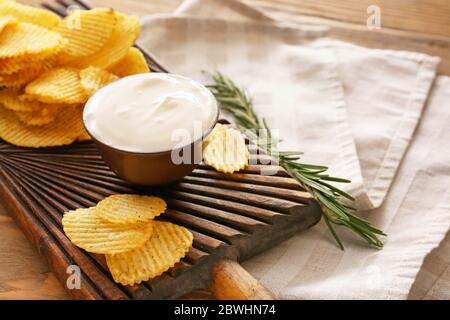 Brett mit schmackhafter saurer Sahne und Kartoffelchips auf dem Tisch Stockfoto