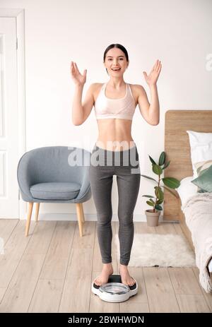 Glückliche junge Frau, die ihr Gewicht zu Hause misst Stockfoto