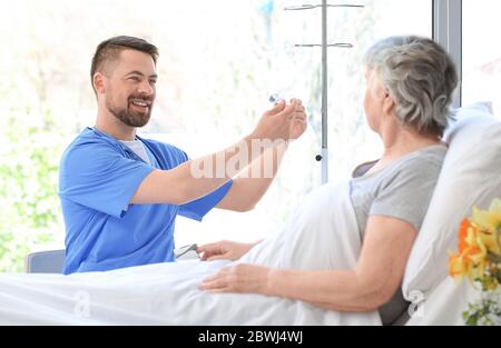 Männlicher Arzt, der mit älteren Patienten im Krankenhauszimmer arbeitet Stockfoto