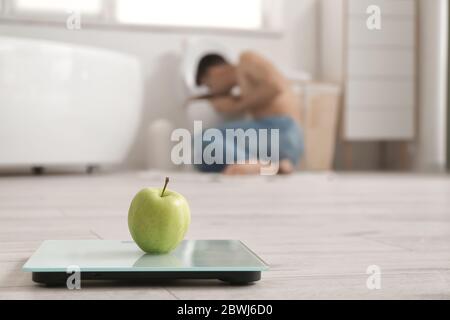 Waage mit Apfel auf dem Boden im Badezimmer. Konzept der Magersucht Stockfoto