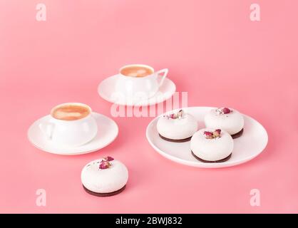 Mousse Gebäck Dessert mit weißer Schokolade mit Rosenblüten und zwei Porzellanbecher Kaffee auf pastellrosa Hintergrund bedeckt. Modern und stilvoll Stockfoto