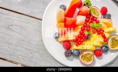 Schüssel mit frischem Obstsalat auf Holzhintergrund, Blick von oben auf Holzschreibtisch. Tropische Früchte, farbenfroher Hintergrund Stockfoto