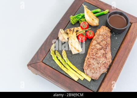 Gegrilltes Rindersteak Fleisch mit Gemüse auf Holzplatte. Luxus-Rindfleisch Steak auf weißem Hintergrund. Rindersteak bereit zum Servieren Stockfoto