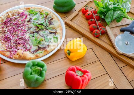 Vegane Pizza und frisches Gemüse auf Holztisch Stockfoto