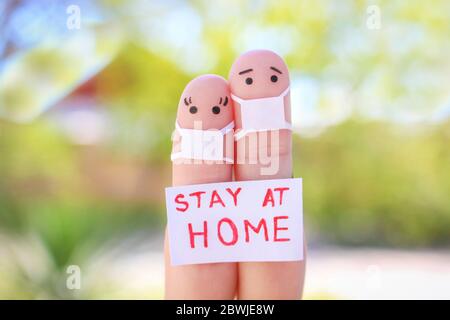 Finger Kunst des Paares mit Gesichtsmaske sitzt in Quarantäne zu Hause. Menschen halten Plakat zu Hause bleiben, um sich vor COVID-2019 zu schützen. Stockfoto