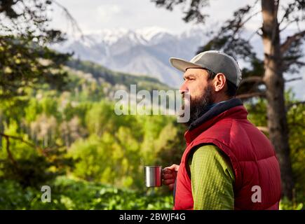 Porträt des bärtigen Touristen ist eine Tasse Kaffee in den üppigen Wald in den Bergen Stockfoto