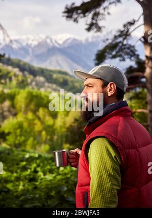 Porträt des bärtigen Touristen ist eine Tasse Kaffee in den üppigen Wald in den Bergen Stockfoto