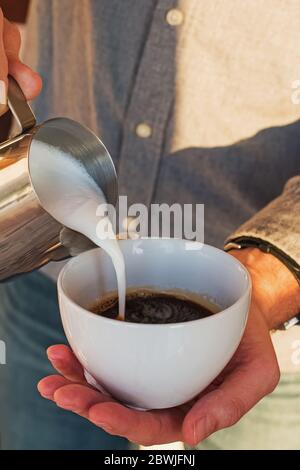 Barista bereitet Cappuccino zu, gießt Milch in Espresso Stockfoto