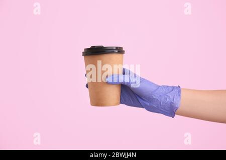 Hand in Handschuh hält Take Away Cup für Getränk auf farbigen Hintergrund Stockfoto