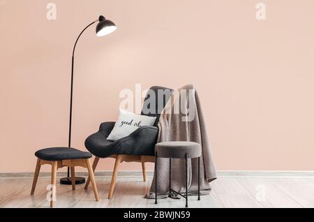 Gemütlicher Sessel mit Lampe in der Nähe von Farbwand im Zimmer Stockfoto