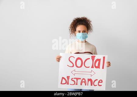 Junge Frau mit Papier mit Text SOZIALE DISTANZ auf grauem Hintergrund. Konzept der Epidemie Stockfoto