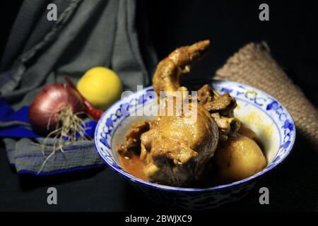 Gekochtes Hühnchen Curry in weißen Topf. Scharf und scharf Chicken Curry mit grüner Zitrone & Chili, Zwiebel isoliert auf schwarzem Hintergrund. Stockfoto