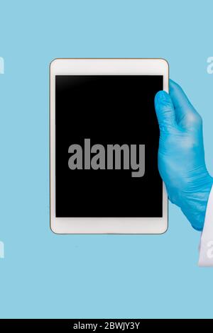Weibliche Hand in einem medizinischen Handschuh hält eine leere moderne Tablette auf einem blauen Hintergrund. Mock-up. Stockfoto