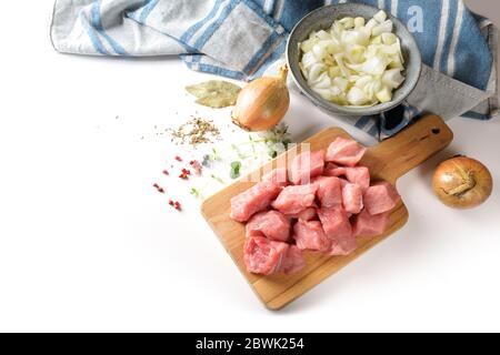 Rohes Schweinefleisch, Zwiebeln, Kräuter und Gewürze, Kochzutaten für einen leckeren Eintopf, Gulasch oder Ragout, auf einem Küchenbrett, isoliert auf einem weißen CO Stockfoto