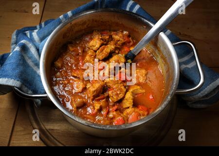 Frisch gekochtes Gulasch oder Eintopf aus Schweinefleisch mit roten Paprika und Zwiebeln in einem Edelstahltopf auf einem rustikalen Holzbrett, ausgewählter Schwerpunkt Stockfoto