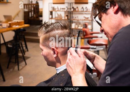 Barbier trimmt die Haare eines jungen Mannes mit einem Rasiermesser in seinem Friseursalon Stockfoto