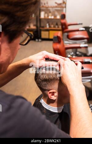 Barbier rasiert in seiner Friseurei mit einer Rasierklinge den Haarstopf eines jungen Mannes Stockfoto