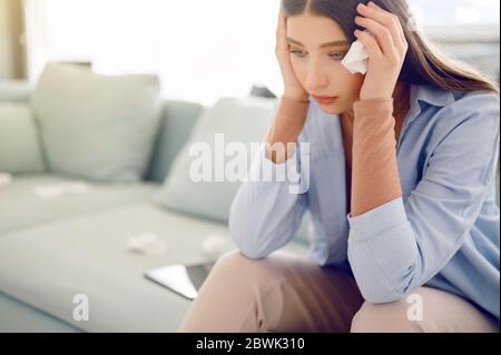 Kranke junge Frau mit Seidenpapier sitzt auf dem Bett, Frau mit Kopfschmerzen, Allergie und Grippe-Konzept Stockfoto