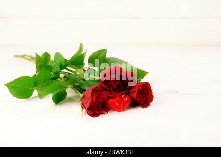 Drei rote Rosen und zwei Herzformen aus Glas auf weißem Holzhintergrund, Liebeskonzept mit Kopierraum, ausgewählter Weichfokus, schmale Tiefe des Fies Stockfoto
