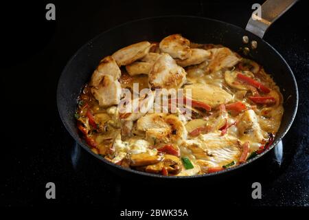 Kochen einer cremigen Chicken Ragout mit Paprika und Pilz in einer Pfanne auf einem schwarzen Herd, kopieren Raum, ausgewählten Fokus, enge Schärfentiefe Stockfoto