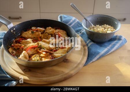 Hähnchenragout mit Paprika und Pilz in einer Pfanne und Blumenkohlreis in einer Schüssel auf einem hölzernen Küchentisch, Kopierraum, ausgewählten Fokus, na Stockfoto