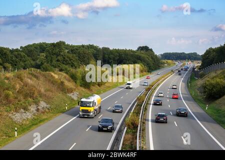 Autos und Lastwagen fahren auf der Autobahn durch eine Landlandschaft, Transport- und Umweltkonzept, blauen Himmel mit Wolken und Kopierraum Stockfoto