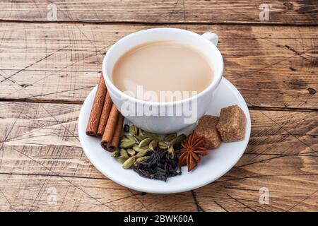 Indischer Tee mit Milch und Gewürzen. Kardamom Sticks Zimt Stern Anis Rohrzucker Holz Hintergrund kopieren Raum. Stockfoto