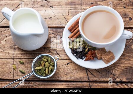 Indischer Tee mit Milch und Gewürzen. Kardamom Sticks Zimt Stern Anis Rohrzucker Holz Hintergrund kopieren Raum. Stockfoto