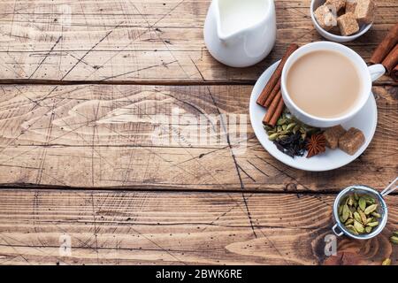 Indischer Tee mit Milch und Gewürzen. Kardamom Sticks Zimt Stern Anis Rohrzucker Holz Hintergrund kopieren Raum. Stockfoto