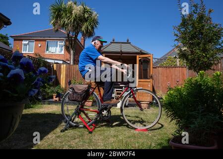 Ältere Paare beide in den 80ern halten sich fit auf einem Fahrradtrainer Stand in ihrem Garten während der Coronavirus Lockdown, Südwestengland, Großbritannien Stockfoto