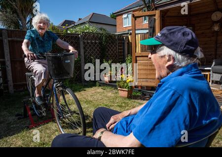 Ältere Paare beide in den 80ern halten sich fit auf einem Fahrradtrainer Stand in ihrem Garten während der Coronavirus Lockdown, Südwestengland, Großbritannien Stockfoto