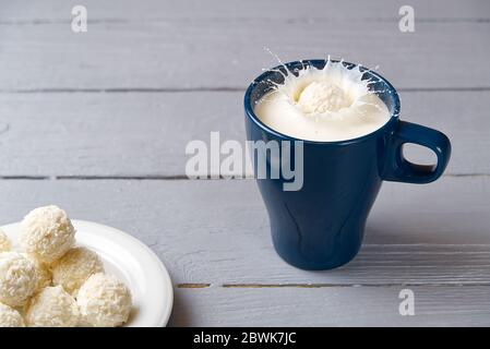 Kokosnusskekse fielen in einen blauen Becher Milch. Spritzer Milch in einen Becher, verursacht durch einen Tropfen Kokosnusstrüffel. Stockfoto