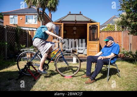 Ältere Paare beide in den 80ern halten sich fit auf einem Fahrradtrainer Stand in ihrem Garten während der Coronavirus Lockdown, Südwestengland, Großbritannien Stockfoto