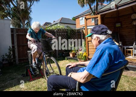 Ältere Paare beide in den 80ern halten sich fit auf einem Fahrradtrainer Stand in ihrem Garten während der Coronavirus Lockdown, Südwestengland, Großbritannien Stockfoto