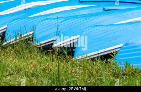 Blaue Fischerboote auf grünem Gras gestapelt. Haufen blauer Boote Stockfoto