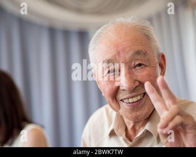 Ein älterer Mann lächelt und zeigt ein Friedenszeichen Stockfoto