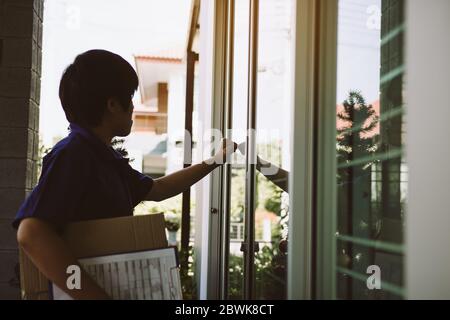 Junge asiatische Kurier ist mit der Hand des Klopfens an der Tür, um die Ware zu liefern. Stockfoto