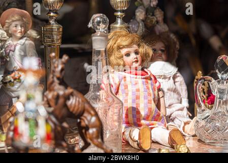 STRASBOURG - APR 28: Vintage gebrauchte Puppe auf dem Flohmarkt mit anderen Dingen: Porzellanfigur, Glaskrug, Kristallkochkanne in Frankreich, Straßburg Stockfoto