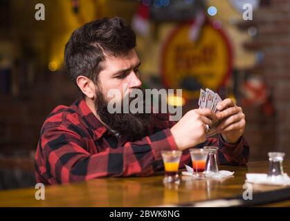 Get Drunk Concept. Guy verbringen Freizeit in Bar trinken Cocktail, defokussed Hintergrund. Mann mit betrunkenem Gesicht sitzen alleine an der Theke. Hipster hält Geld, zählen Bargeld, um mehr Alkohol zu kaufen. Stockfoto