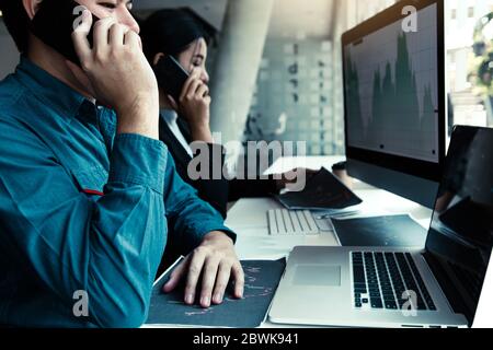 Zwei asiatische Agenten Mann arbeitet und Analyse zusammen in Büro Markt Finanzdiagramme und Grafiken und Anrufe an den Kunden. Stockfoto