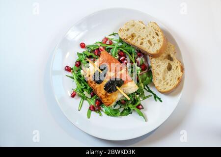 Gebratenes Hähnchen Saltimbocca mit Schinken und Salbeiblättern umwickelt, serviert auf Rucola-Salat und mit Brot auf einem Teller auf einem weißen Tisch, Kopierraum, Stockfoto