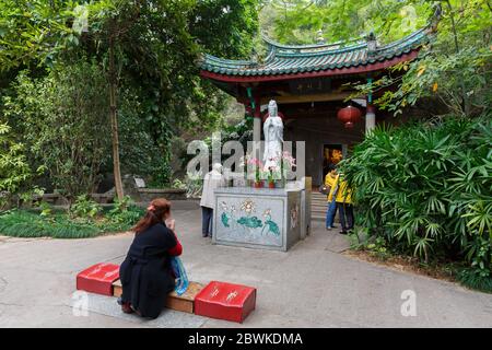 Frau, die vor einer weißen Guanyin Statue betet. Im Nanputuo Tempel Park. Stockfoto